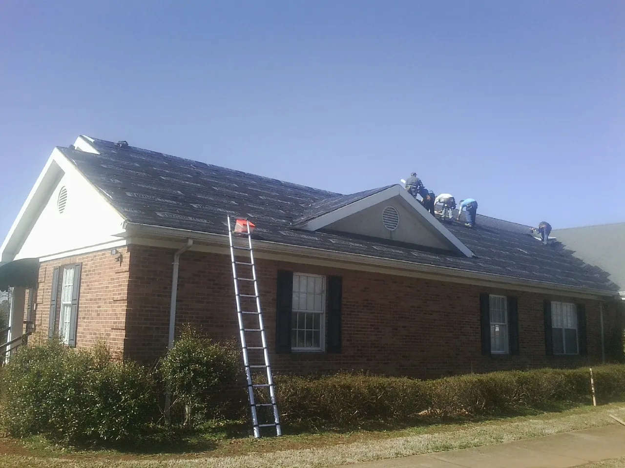 Crew tearing shingles off a brick ranch roof with a ladder set — Emergency Roof Repair work by our crew in Monrovia